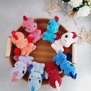 Puede incluir: Una colección de ocho juguetes de peluche tejidos a crochet en una variedad de colores, incluyendo rosa, azul, naranja, morado y rojo. Los juguetes están dispuestos en círculo sobre una cesta de mimbre.