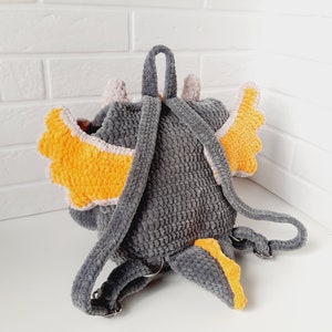 May include: Gray crocheted backpack with orange and white wings and a tail. The backpack has adjustable straps.
