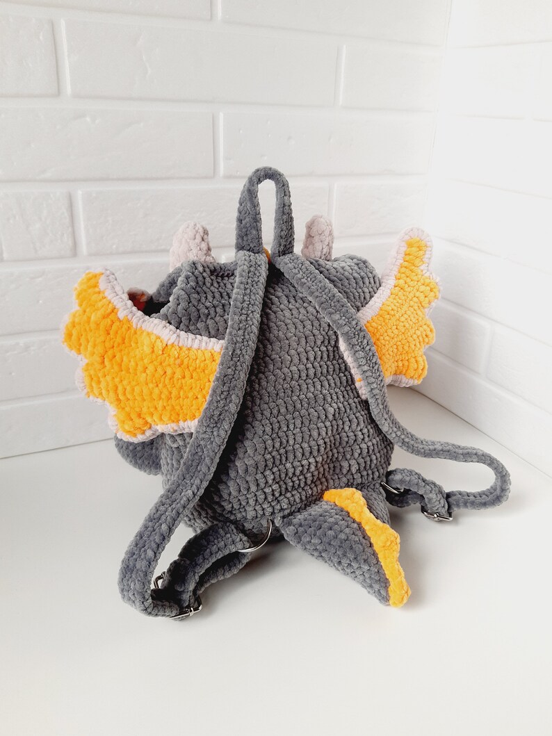 May include: Gray crocheted backpack with orange and white wings and a tail. The backpack has adjustable straps.