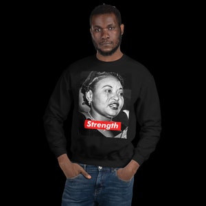May include: Black sweatshirt with a black and white image of a woman speaking. The image is framed by a red rectangle with the word "Strength" in white letters.