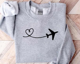 May include: Gray sweatshirt with a black airplane and heart design. The airplane is flying away from a heart.
