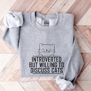 May include: Grey sweatshirt with a black cat illustration and the text "Introverted but willing to discuss cats".