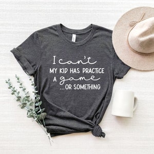May include: A dark gray t-shirt with the text "I can't my kid has practice a game... or something" printed in white.