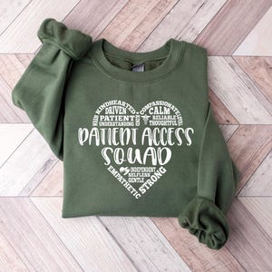 May include: Green sweatshirt with a white heart-shaped graphic that says "Patient Access Squad" and lists positive qualities like "kindhearted", "driven", "calm", "compassionate", "reliable", "understanding", "thoughtful", "independent", "selfless", "strong", "gentle", and "empathetic".
