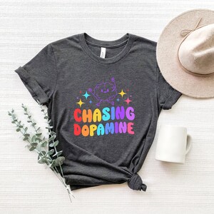 May include: A dark gray t-shirt with a rainbow graphic of a cartoon brain with the text "Chasing Dopamine".
