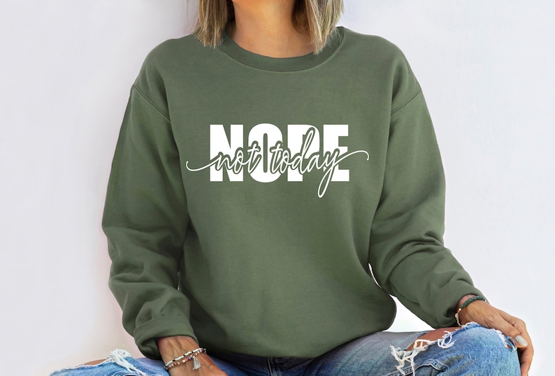 Puede incluir: Sudadera verde oliva con el texto blanco "NOPE not today". La palabra "NOPE" est&aacute; en negrita, con "not today" en escritura cursiva. La sudadera es de cuello redondo.