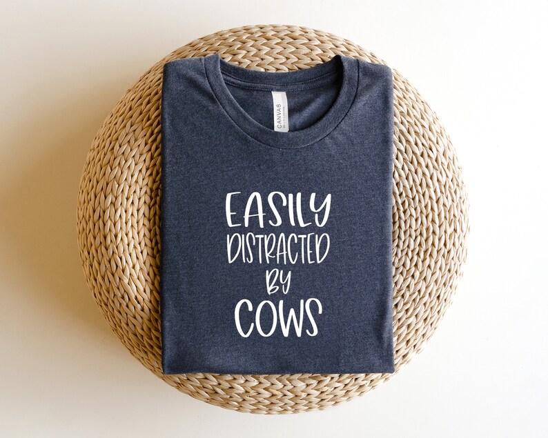 Pu&ograve; includere: Una maglietta grigia scura con la scritta "Easily Distracted by Cows" stampata in bianco.