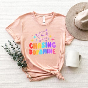 May include: A pink t-shirt with a rainbow graphic of a brain with the text "Chasing Dopamine".
