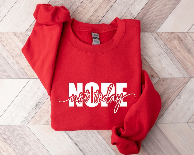 Puede incluir: Una sudadera roja brillante con la palabra "NOPE" en letras blancas grandes y las palabras "not today" en una fuente cursiva. La sudadera est&aacute; doblada, con las mangas visibles.