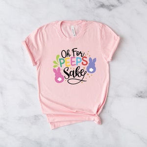 May include: Pink t-shirt with a graphic that says "Oh For Peeps Sake" with colorful bunny illustrations.