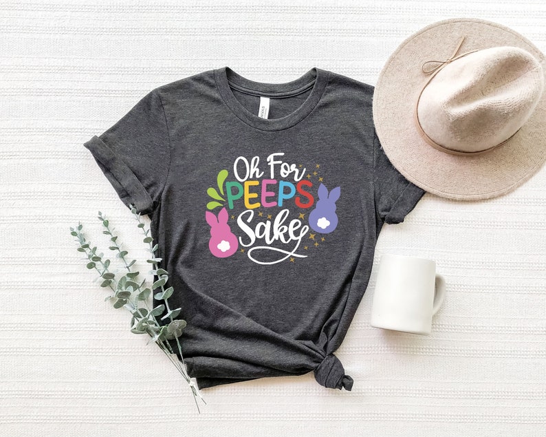 May include: A dark grey t-shirt with the text "Oh For Peeps Sake" in colorful letters and a pink bunny graphic.