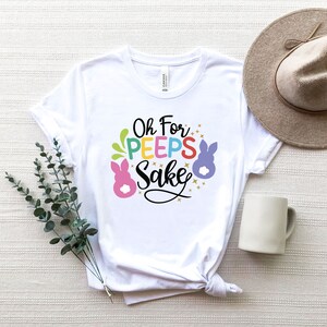 May include: White t-shirt with the text "Oh For Peeps Sake" in colorful letters and a cartoon bunny graphic.