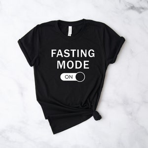 May include: Black t-shirt with white text that reads "FASTING MODE ON" with a white toggle switch graphic.