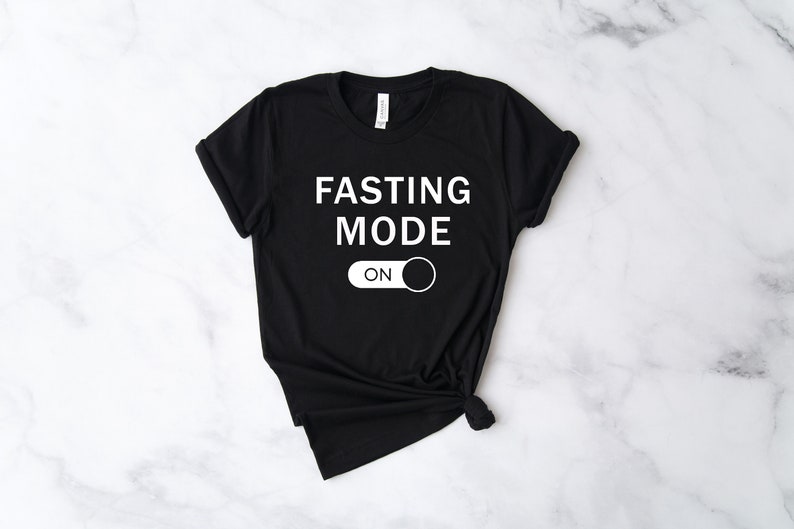 May include: Black t-shirt with white text that reads "FASTING MODE ON" with a white toggle switch graphic.