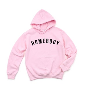 Peut inclure: Sweat-shirt &agrave; capuche rose avec le texte "HOMEBODY" en lettres noires.