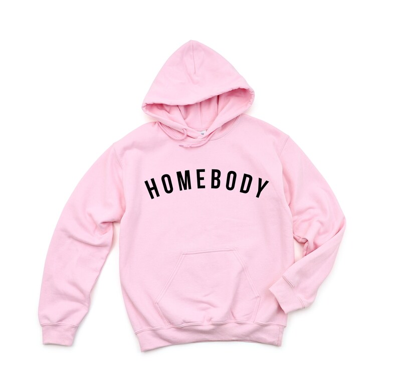 Peut inclure: Sweat-shirt &agrave; capuche rose avec le texte "HOMEBODY" en lettres noires.