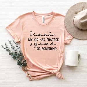 May include: A peach-colored t-shirt with the text "I can't my kid has practice a game... or something" printed in black.