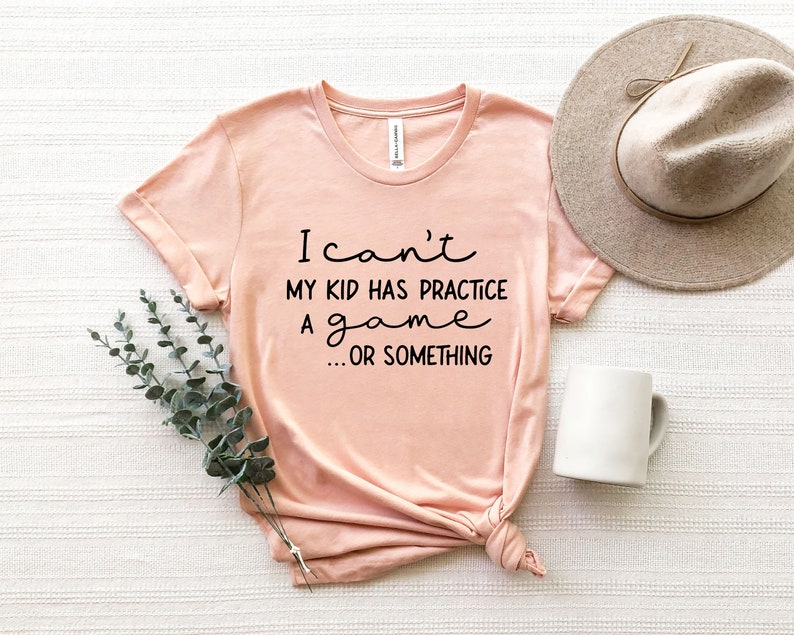 May include: A peach-colored t-shirt with the text "I can't my kid has practice a game... or something" printed in black.