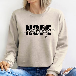 Puede incluir: Sudadera beige con la frase "NOPE not today" en negro. La palabra "NOPE" est&aacute; en negrita, sin serifa, mientras que "not today" est&aacute; en cursiva. La sudadera es de estilo casual.