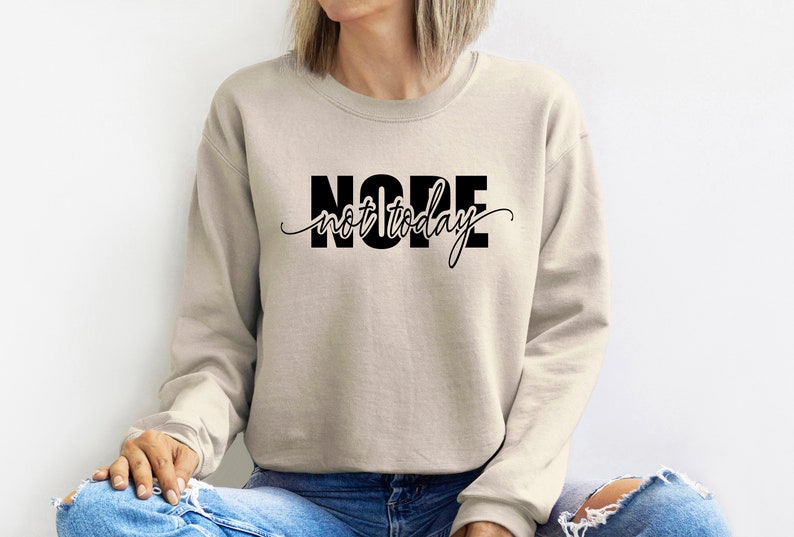Puede incluir: Sudadera beige con la frase "NOPE not today" en negro. La palabra "NOPE" est&aacute; en negrita, sin serifa, mientras que "not today" est&aacute; en cursiva. La sudadera es de estilo casual.
