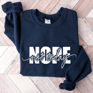 Puede incluir: Una sudadera azul marino con las palabras "NOPE" en letras blancas grandes y "not today" en cursiva. La sudadera tiene cuello redondo y mangas largas con pu&ntilde;os acanalados.