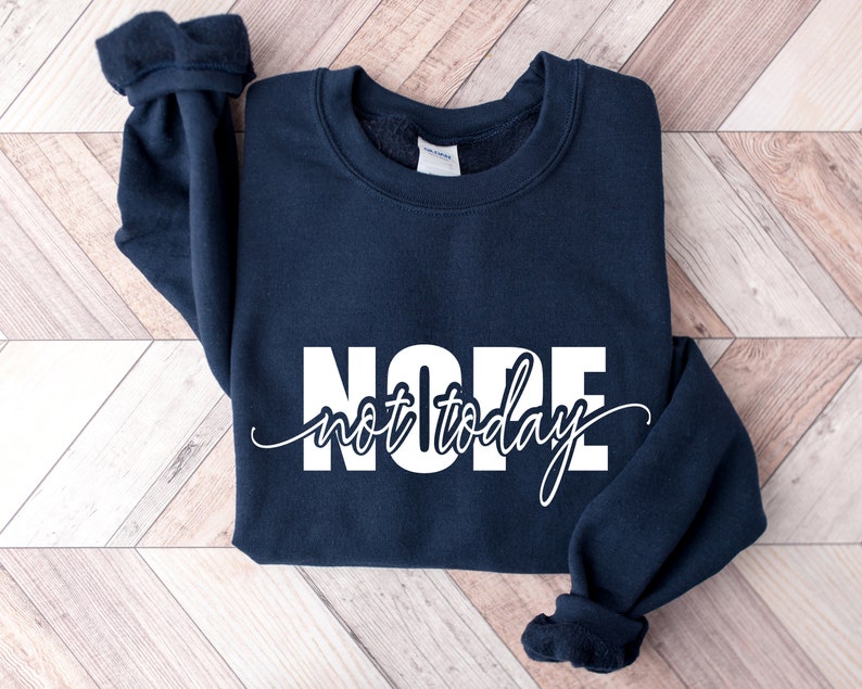 Puede incluir: Una sudadera azul marino con las palabras "NOPE" en letras blancas grandes y "not today" en cursiva. La sudadera tiene cuello redondo y mangas largas con pu&ntilde;os acanalados.