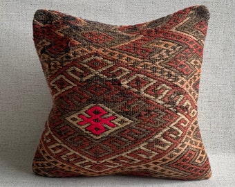 May include: A brown and red patterned throw pillow with a pink geometric design in the center.