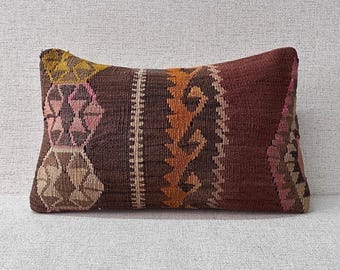 May include: Rectangular decorative pillow with a woven design. The pillow features a mix of colors, including brown, burgundy, yellow, and pink. The pattern includes geometric shapes and vertical stripes, suitable for home decor.