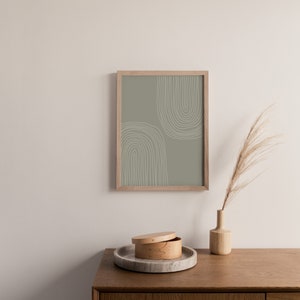 May include: A framed print with a sage green background and white arched lines. A wooden vase with dried grass and a round wooden box with a lid sit on a wooden cabinet. A marble tray holds the box.