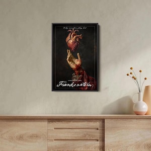 Op de afbeelding: Ingelijste kunstdruk met een menselijk hart boven een hand, met het woord "Frankenstein" in witte letters. Het kunstwerk heeft een donkere, gotische esthetiek, met de tekst "Only monsters play God" bovenaan.