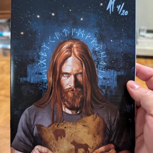 May include: A comic book cover featuring a long-haired, bearded person holding a piece of parchment with animal silhouettes. The background is a dark, starry night sky with a glowing blue runic inscription. A signature and date are in the top right.