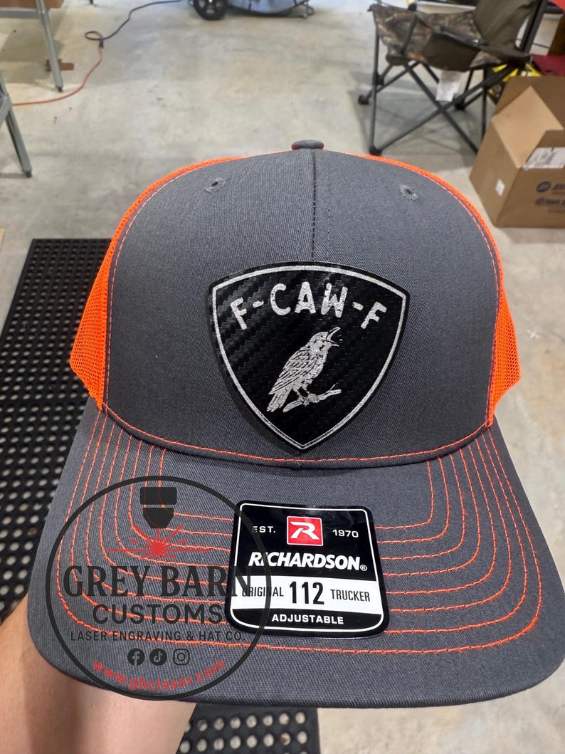 May include: A gray and orange trucker hat with a patch that reads "F-CAW-F" and a bird illustration. The hat has orange stitching and a mesh back. The tag reads "RICHARDSON 112 TRUCKER ADJUSTABLE".