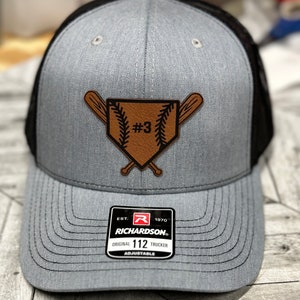 May include: A grey and black baseball cap with a brown leather patch featuring a baseball diamond, two crossed bats, and the number "#3". The cap is adjustable and has the Richardson logo on the side.