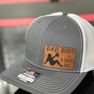 May include: Gray and white trucker hat with a brown leather patch that says "Dad Bods & A Small Rod".