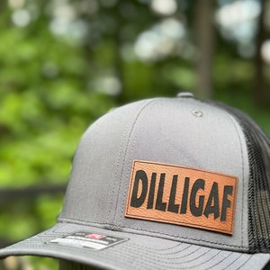 May include: A gray and black trucker hat with a brown leather patch that says "DILLIGAF" in black lettering.