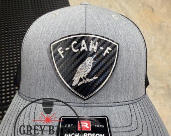 May include: A gray trucker hat with a black mesh back. The front features a patch with the text "F-CAN-F" and a bird illustration. A tag reads "RICHARDSON® ORIGINAL 112 TRUCKER ADJUSTABLE". The hat is from Grey Barn Custom.