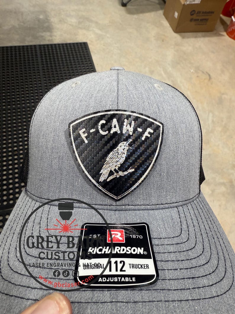 May include: A gray trucker hat with a black mesh back. The front features a patch with the text "F-CAN-F" and a bird illustration. A tag reads "RICHARDSON&reg; ORIGINAL 112 TRUCKER ADJUSTABLE". The hat is from Grey Barn Custom.