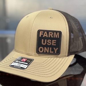 May include: A tan and brown trucker hat with a mesh back. The front of the hat has a square patch with the words "FARM USE ONLY" in white. The hat also has a Richardson tag.