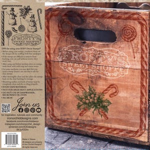 May include: A vintage-style wooden crate with a white "Frosty's Sweet Shoppe" logo and red candy cane designs. The crate is surrounded by a brown paper background with a black and white illustration of a snowman and candy canes. The text "Tips for using your IOD Decor Stamps" is printed on the paper.