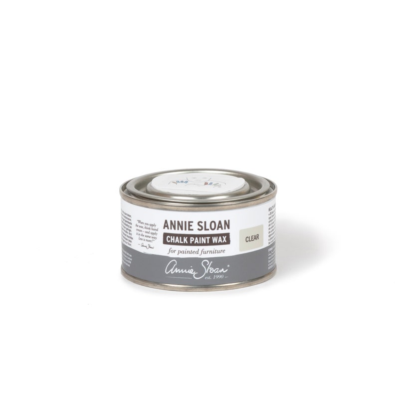May include: A silver tin of Annie Sloan Chalk Paint Wax in the color Clear. The tin has a white label with black text that reads "Annie Sloan Chalk Paint Wax for painted furniture".