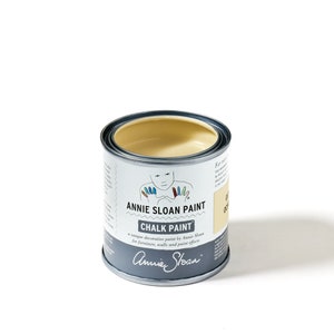 May include: A small can of Annie Sloan Chalk Paint in the color Old Ochre. The can is white with black lettering and a cartoon illustration of a person with colorful hands.