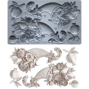 May include: A gray silicone mold featuring intricate relief designs of two cornucopias filled with flowers, pumpkins, and pomegranates, along with individual pomegranate motifs. The text "CORNUCOPIAS IOD" is embossed on the mold surface.