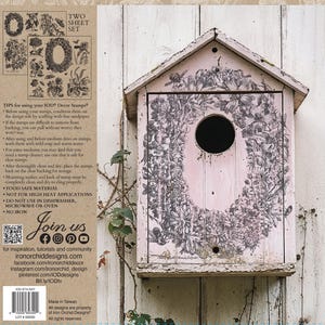 May include: A weathered, pink birdhouse with a floral wreath design around a circular opening. The birdhouse is mounted on a white wooden surface. The image also shows a two-sheet stamp set with floral designs.