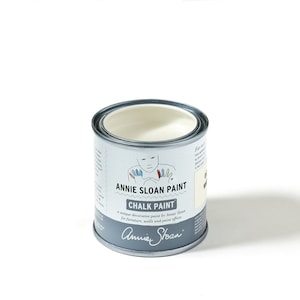 May include: A white can of Annie Sloan Chalk Paint. The can has a label with a cartoon illustration of a child with painted hands and the text "Annie Sloan Paint Chalk Paint a unique decorative paint by Annie Sloan for furniture, walls and paint effects Annie Sloan".