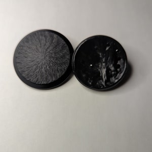 May include: Two black round buttons, one with a smooth surface and the other with a textured surface.