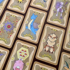 Peut inclure: Un jeu de cartes de tarot avec des personnages Pokémon. Chaque carte présente une illustration de Pokémon et un nom de carte de tarot, tels que "L'Étoile", "Le Chariot" et "Le Diable".