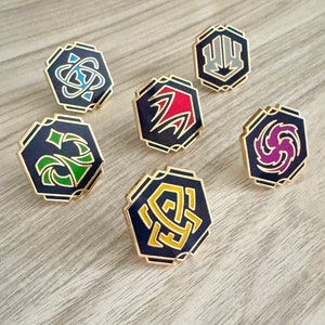 Puede incluir: Seis pines hexagonales de esmalte con diferentes diseños. Cada pin presenta un símbolo de color diferente sobre un fondo negro. Los pines son de color dorado y tienen un acabado brillante.