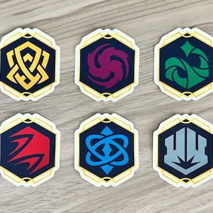 Peut inclure: Six autocollants hexagonaux avec différents symboles et couleurs. Les symboles sont un nœud, un tourbillon, une feuille, une double flèche, un nœud et un bouclier. Les couleurs sont or, violet, vert, bleu, or et gris.