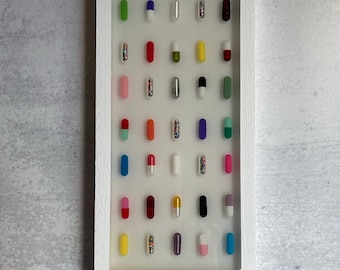 May include: A white frame with a clear background displaying a collection of colorful capsules. The capsules are arranged in rows and columns, and each capsule is filled with different colored beads.