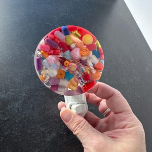 May include: A white night light with a round, clear resin top filled with colorful pills and capsules. The light switch is on the side of the base.